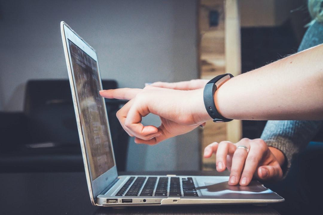 A closeup of two people working on a laptop and pointing at the screen.